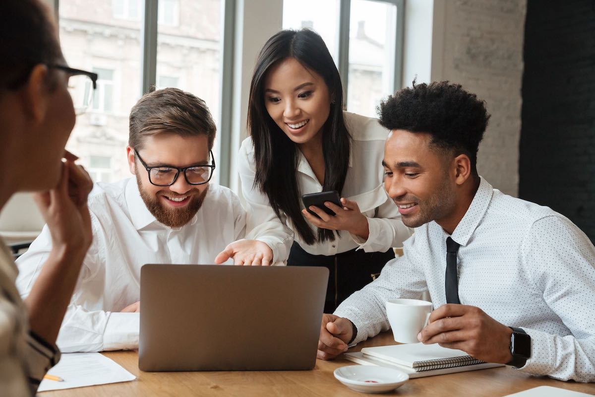 Happy office coworkers huddling over web design on laptop