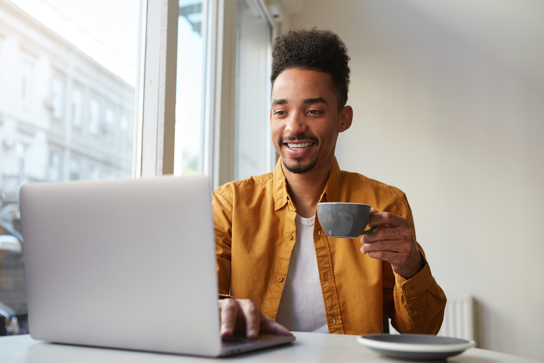 Black Man On His Laptop Reading An Article About How To Build A Wordpress Site From Scratch And Holding A Cup Of Coffee