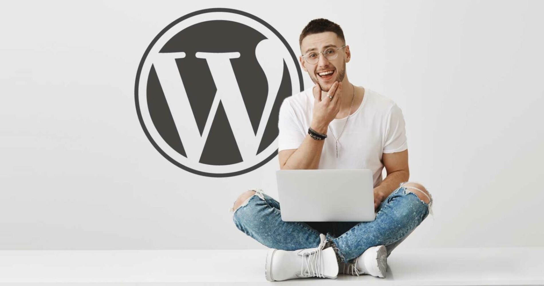 Cross legged man sitting with laptop in front of a white wall designing custom Wordpress website design. On the wall is a large WordPress logo.