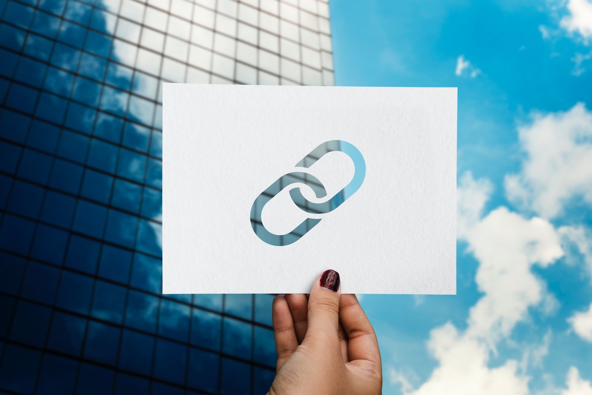 Woman’s Hand Holding Up A Paper With A Link Symbol Representing Backlink As One Of The Seo Terms For Beginners