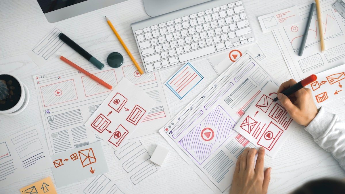 Web Designer Hand Drawing Mockups Of User Friendly Web Page Layouts In Marker On Busy Desk