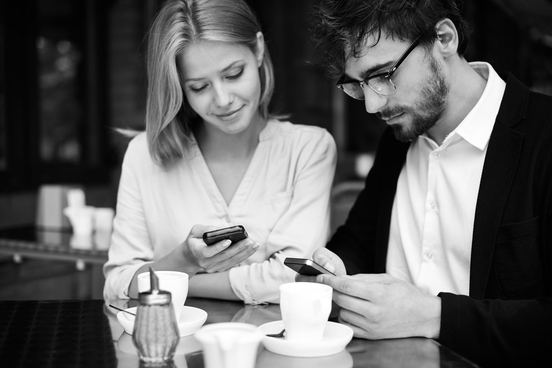Man And Woman At A Café Looking At Smartphones And Browsing Websites Over Coffee